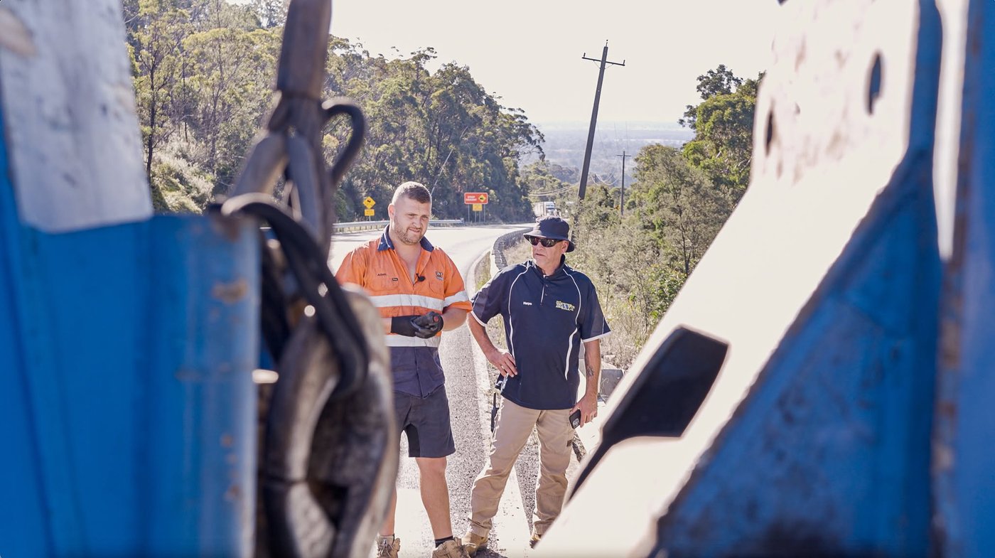 Two KWT operators talking through a job on the roadside, framed by the wrecker boom