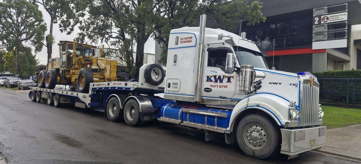 KWT prime mover transporting a road grader on a low loader trailer