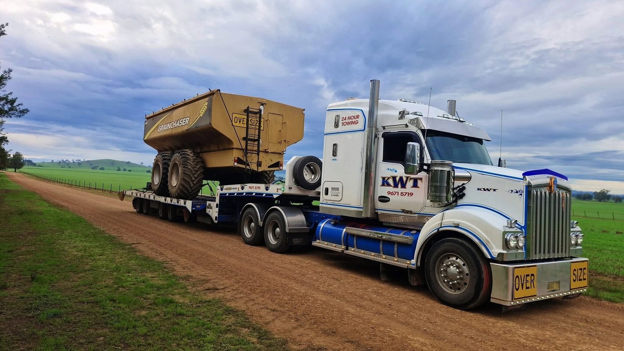 KWT Kenworth hauling an oversize Grainchaser bin on a low loader down a country road