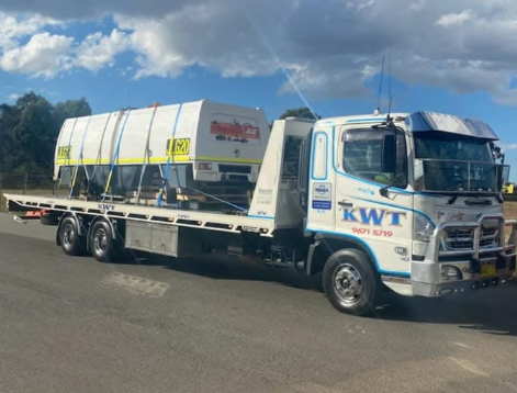 KWT flatbed towing a car through the city