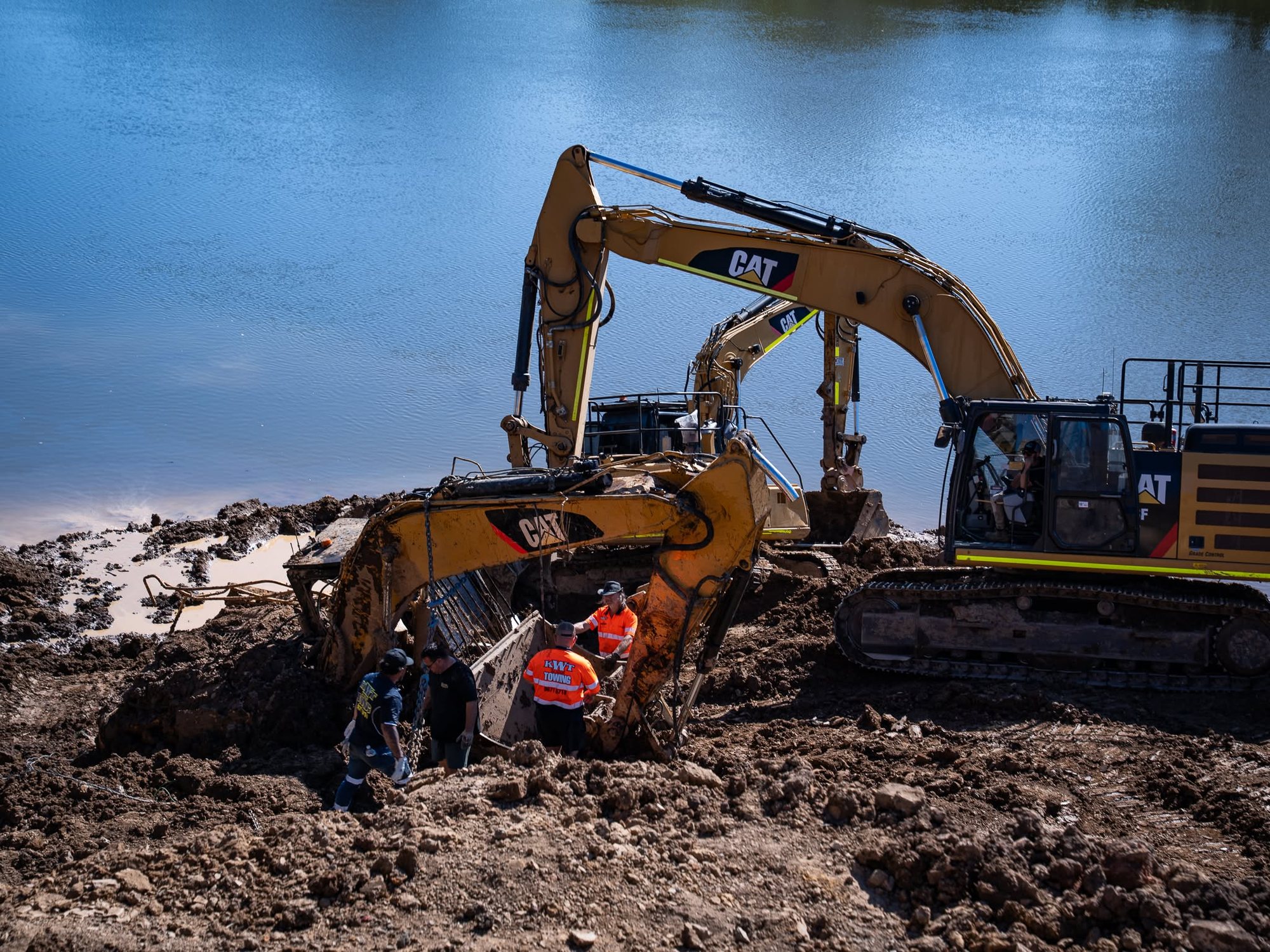 KWT crew using a CAT excavator and winch line to recover heavy machinery bogged at a riverbank